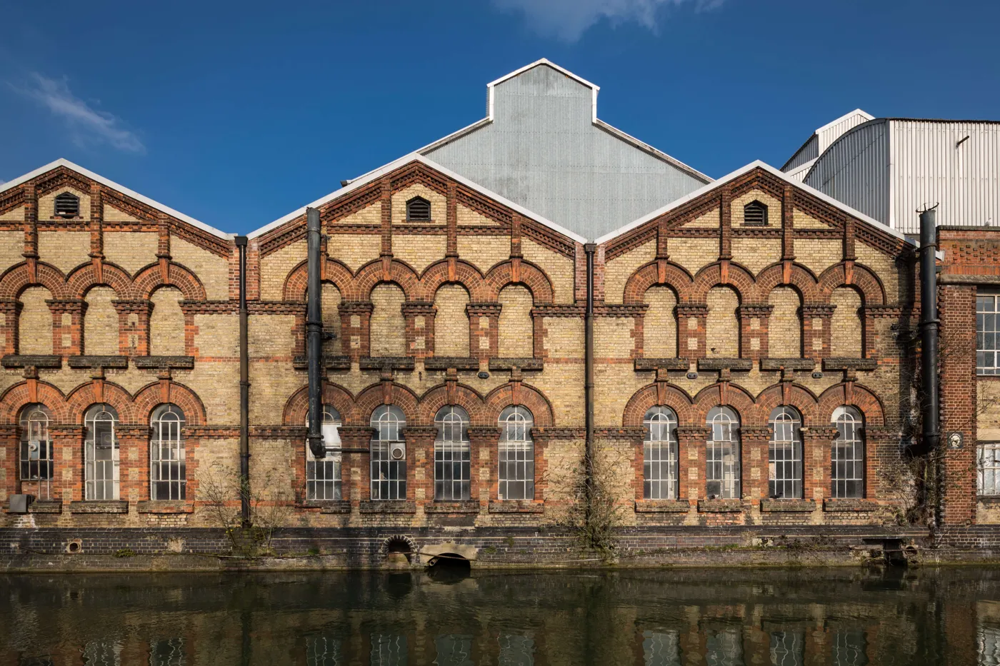 The Osney Power Station brick frontage on the river before redevelopment, with three gabled bays and rows of arched windows